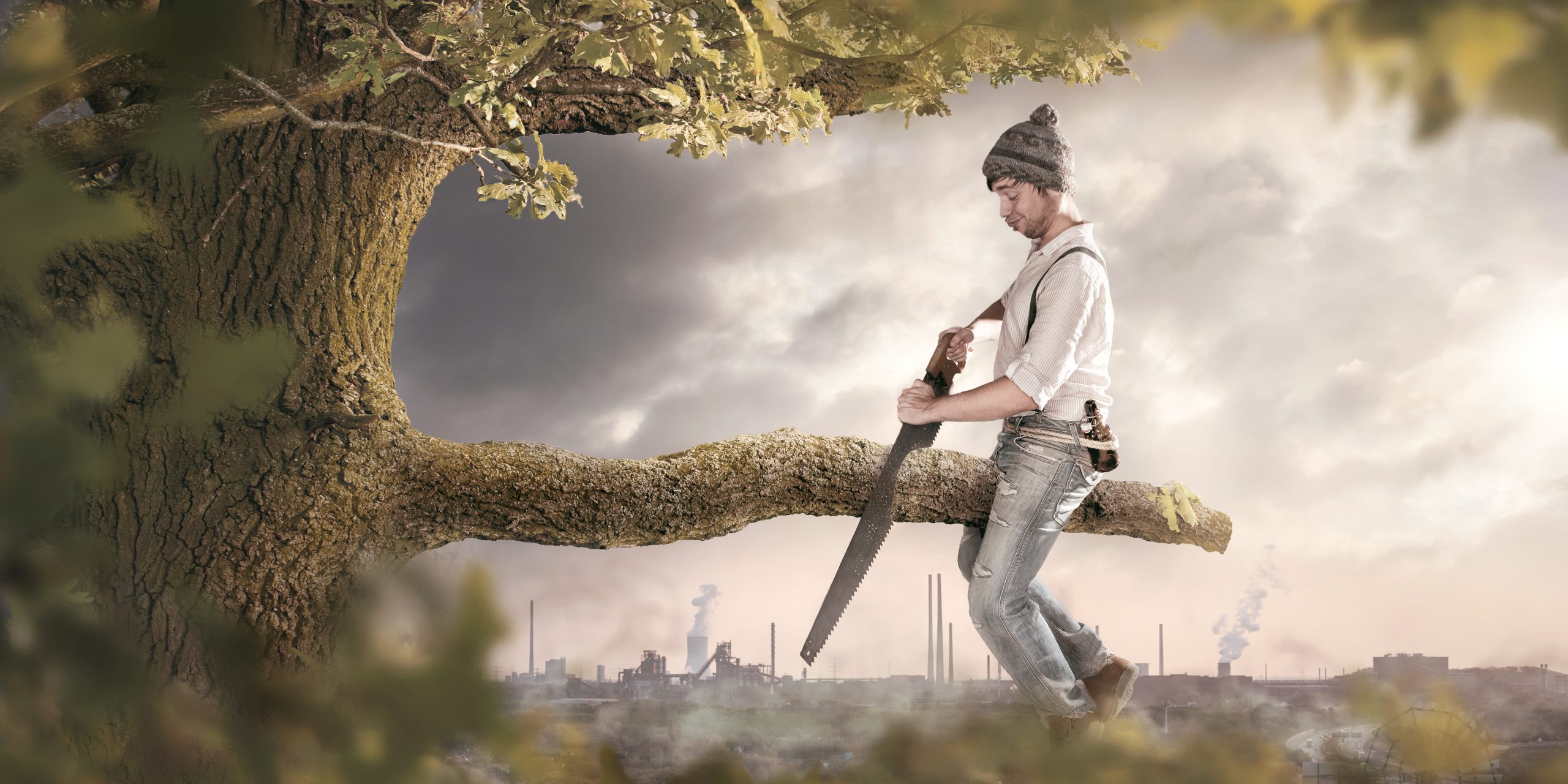 A man is sitting on a branch he is about to cut off. The background shows an industrial area which is polluting the surroundings. Thus the image conveys a secondary meaning towards environmental pollution.